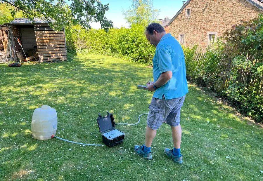 Stéphane Wilkin réalisant un test de perméabilité dans un jardin, cuve et appareil de mesure